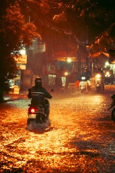 A person riding a motorbike through a rain-drenched city street illuminated by streetlights at night.