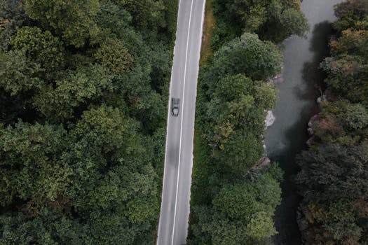Drone shot of a lone car on a winding road through dense forest and beside a serene river in Kemerköprü, Türkiye.