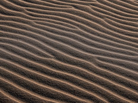High-angle view of wavy sand patterns in a barren desert setting, creating a textured natural background.