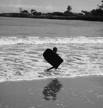 Young boy running with a bodyboard at the beach, captured in black and white.