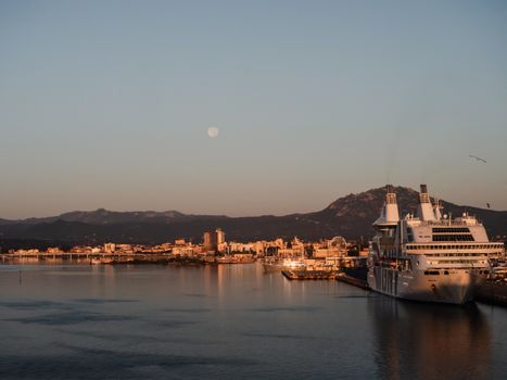 Captivating view of Olbia harbor with cruise ship and full moon at dusk in Sardinia, Italy.