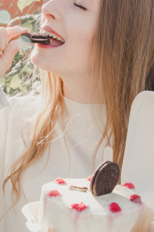 Woman Eating a Cookie from a Cream Cake Topped with Sandwich Biscuits