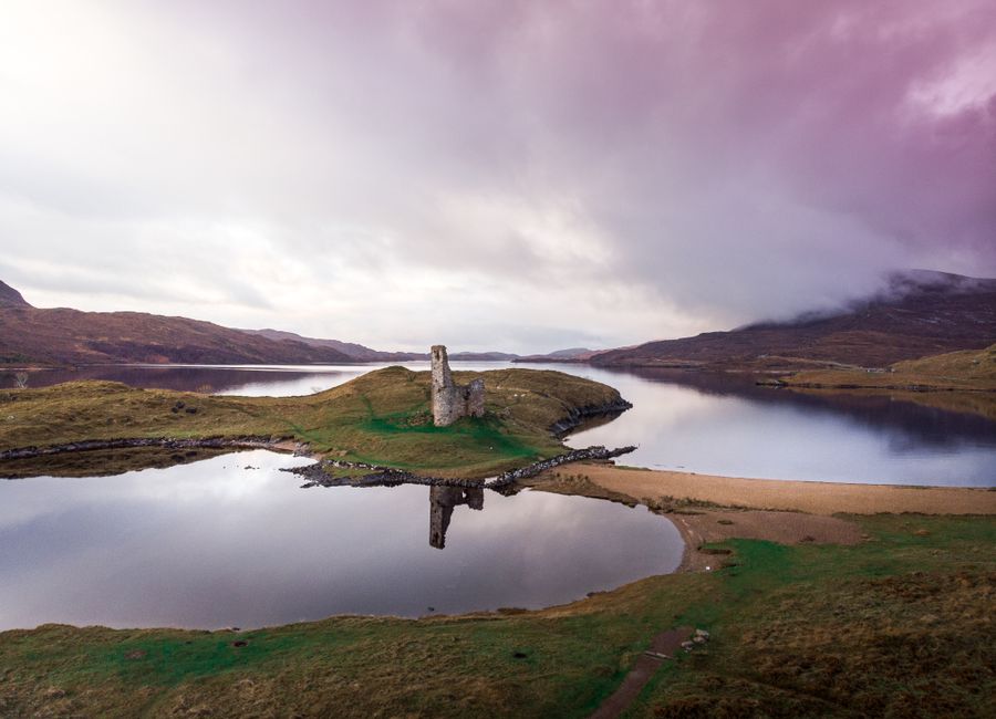 Aerial view of Ardvreck Castle reflecting on a tranquil lake in Lairg, Scotland.