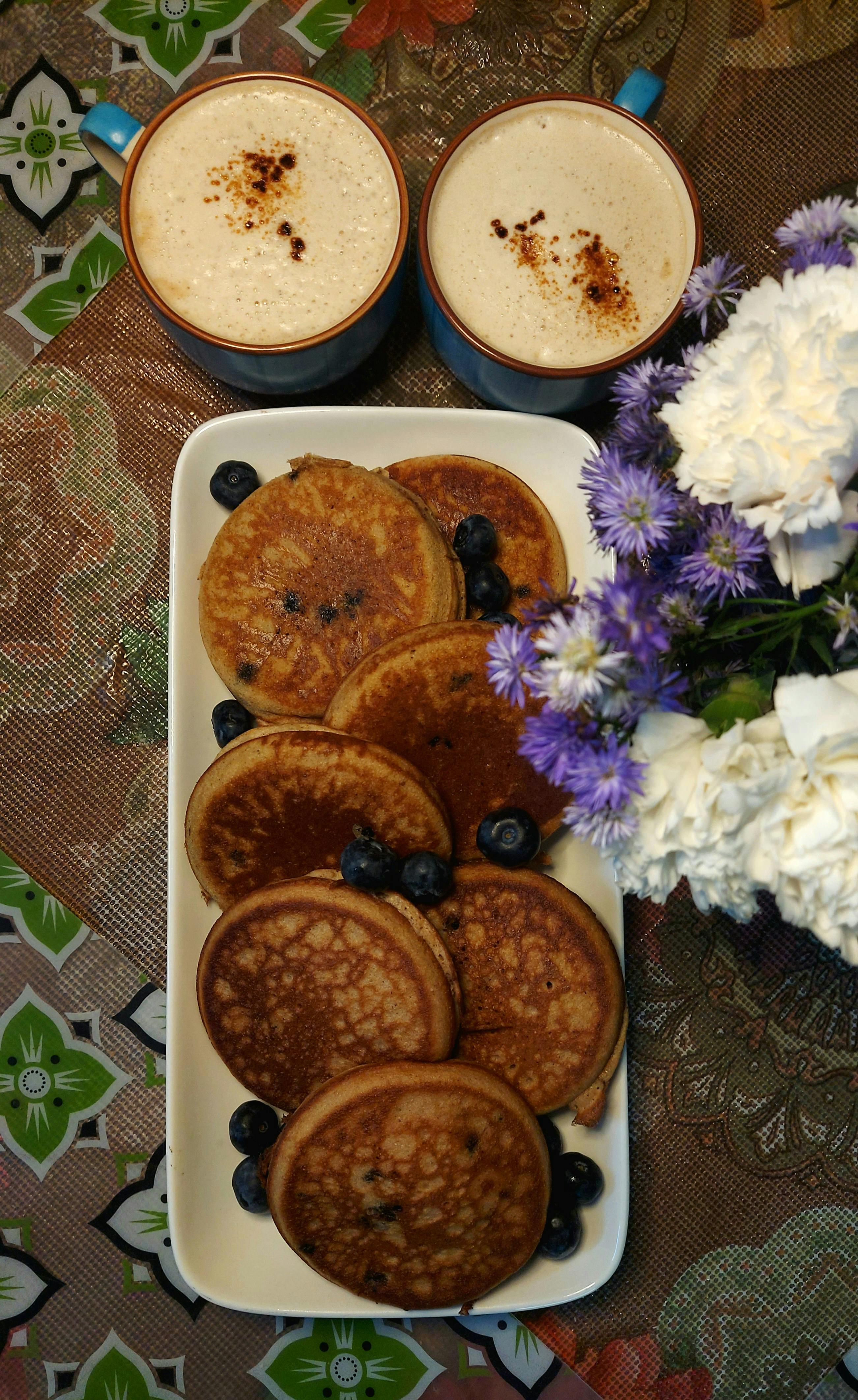 Blueberry Pancakes and Cappuccino on the Table Next to the Vase with Flowers