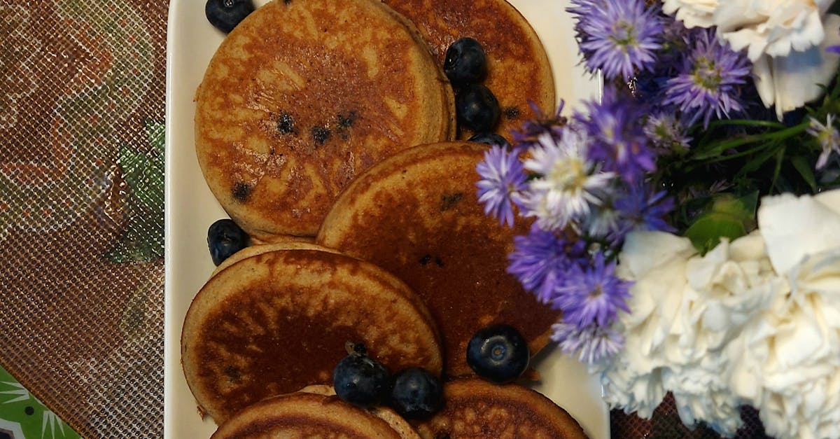 Blueberry Pancakes and Cappuccino on the Table Next to the Vase with Flowers