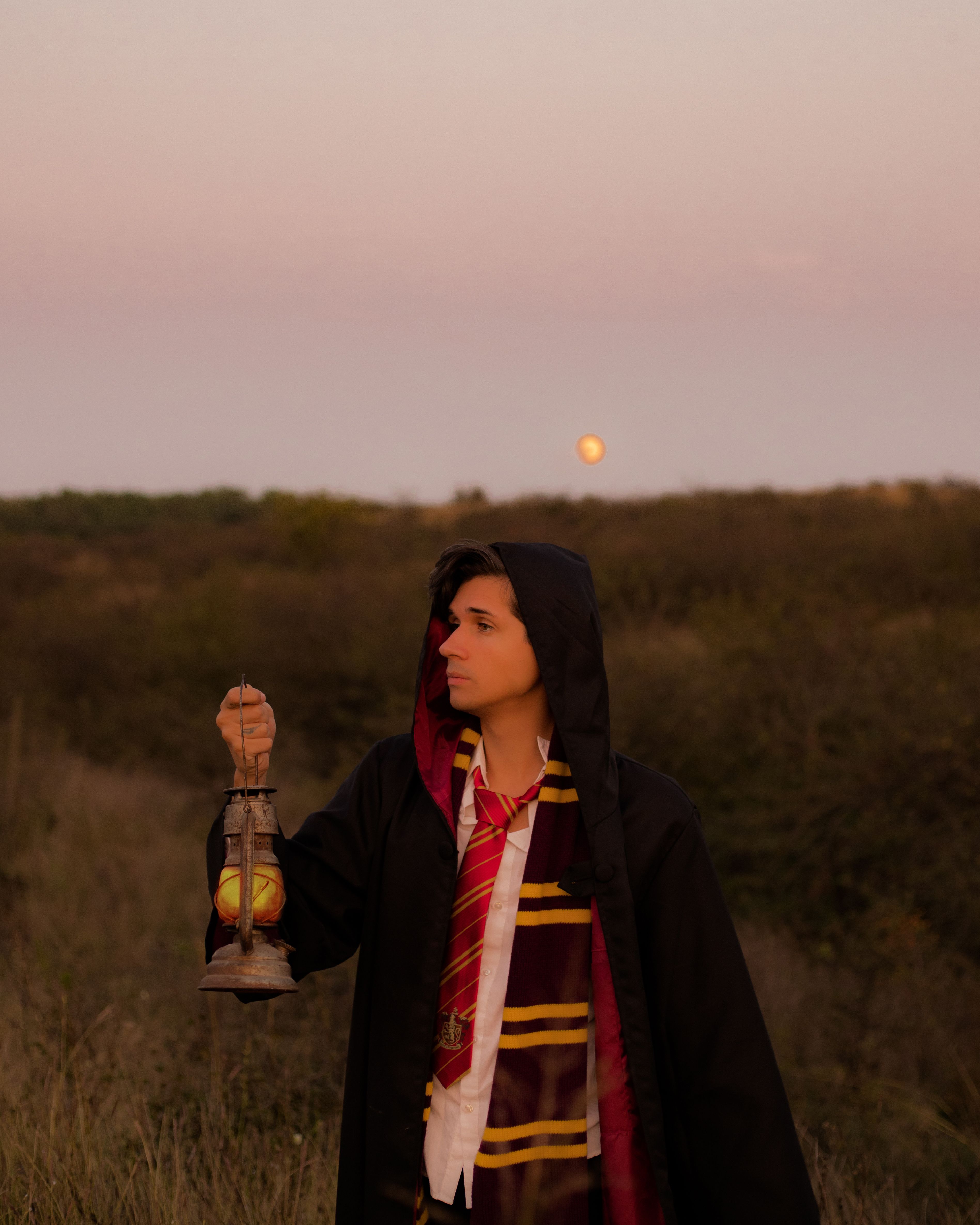 Person dressed in wizard costume holding lantern in a twilight field