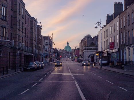 A serene Dublin city street at sunrise with cars and iconic architecture featuring a dome.