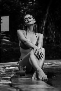 Stylish woman in a bikini posing by a swimming pool, enjoying a relaxing moment.
