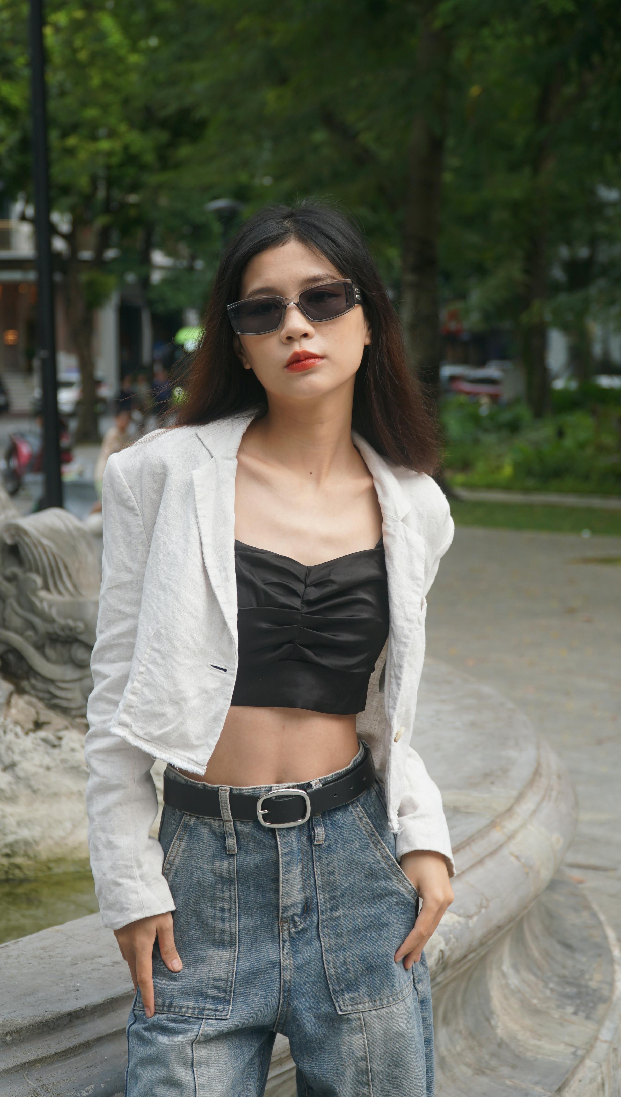 Fashionable woman poses confidently in an urban park with trees and people in the background.