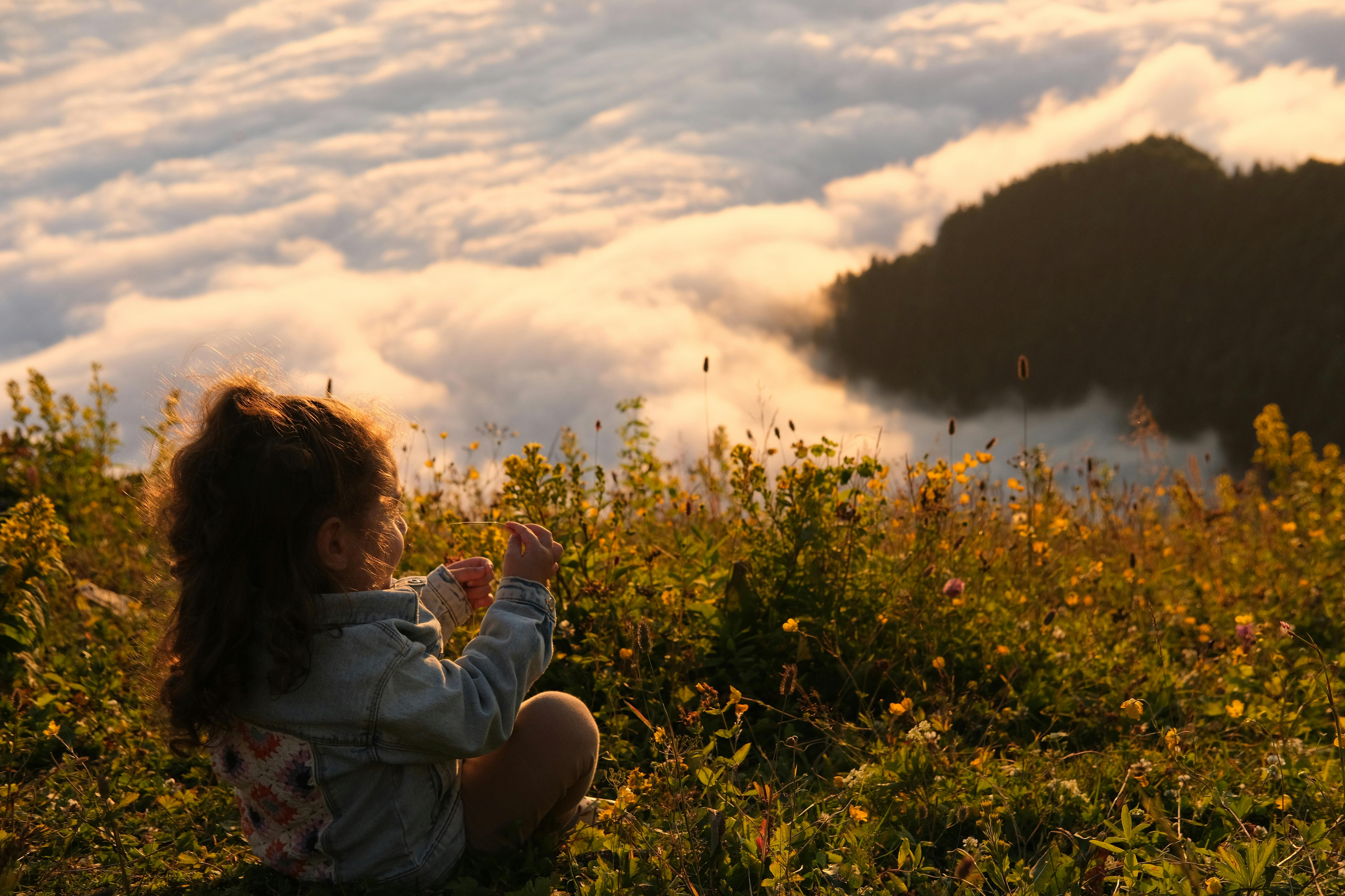 a little girl sitting on a mountain peak above the clouds