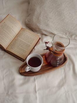 Top view of a cozy bed with a cup of coffee, book, and carafe on a tray for a relaxing morning.