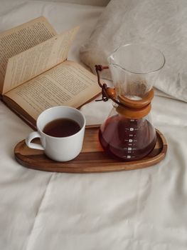 Top view of a coffee setup on bed with an open book and a wooden tray.