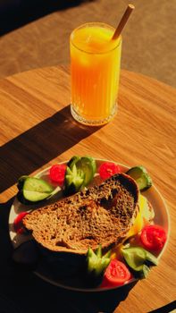 Rustic sandwich with vegetables and fresh orange juice on a sunny table.