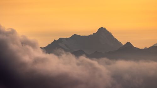 Free Serene view of majestic mountain peaks surrounded by clouds during a vibrant sunset. Stock Photo