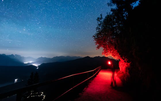 A captivating night hiking scene in the Alps with a starry sky and red torchlight.