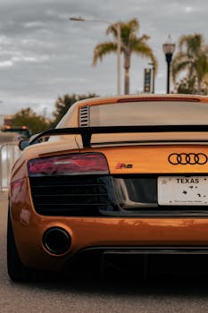 Gold Audi R8 sports car with spoiler and visible Texas license plate parked on city street.