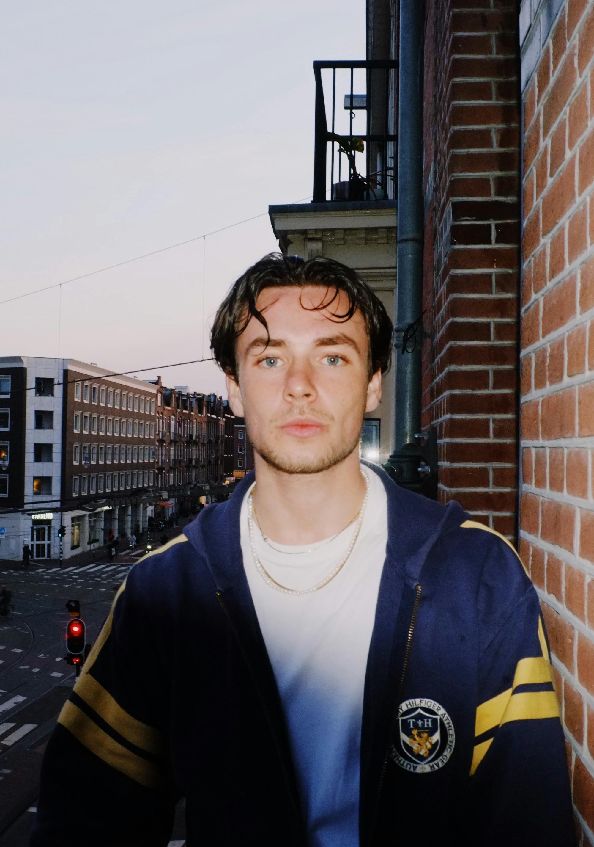 Portrait of a young man standing on a city balcony at dusk, capturing a calm urban atmosphere.