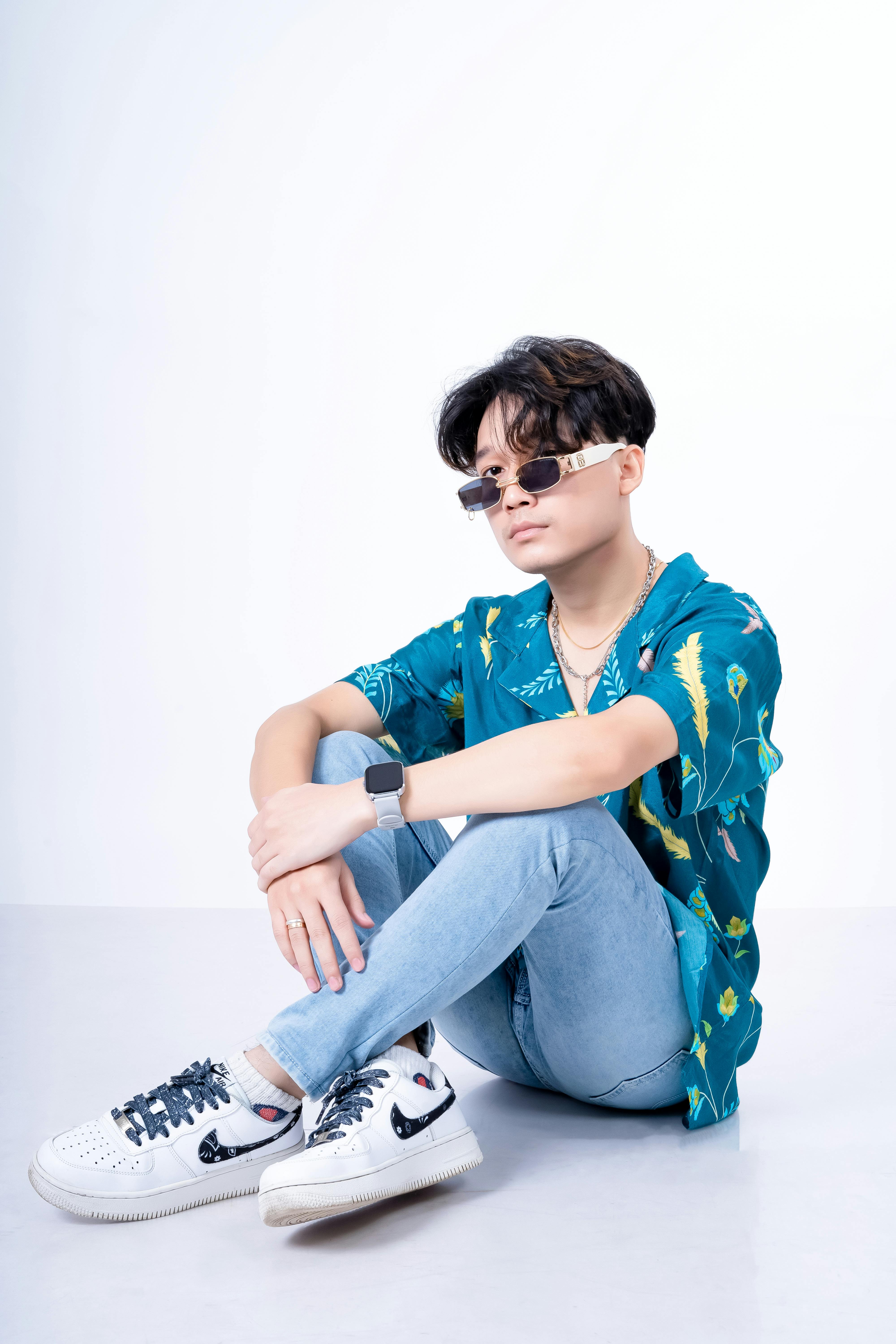 A fashionable young man in sunglasses, sitting casually in a studio, exuding a cool style.