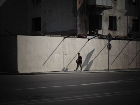 A man strolls along a dimly lit street in Baku, Azerbaijan, casting shadows on a sunny day.