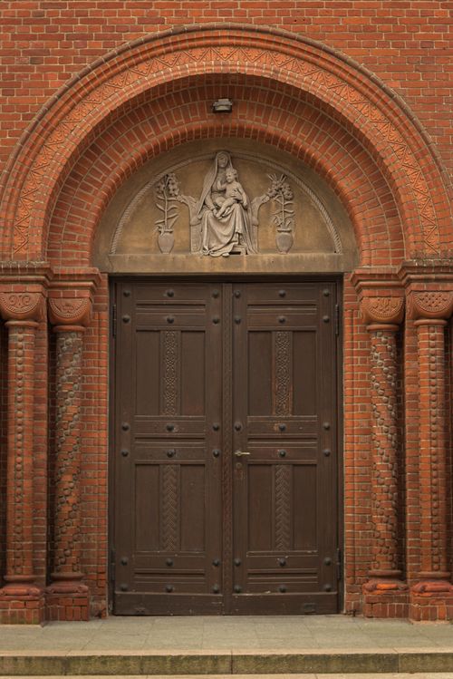 Free Intricate wooden church doors framed by ornate brickwork and religious relief sculpture. Stock Photo