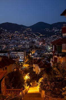 Aerial view of Alanya cityscape in Türkiye at twilight, showcasing hills and city lights.