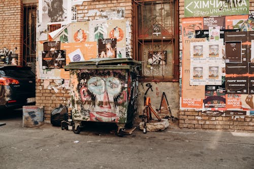 Posters on Wall over Garbage Bin in Alley in Town