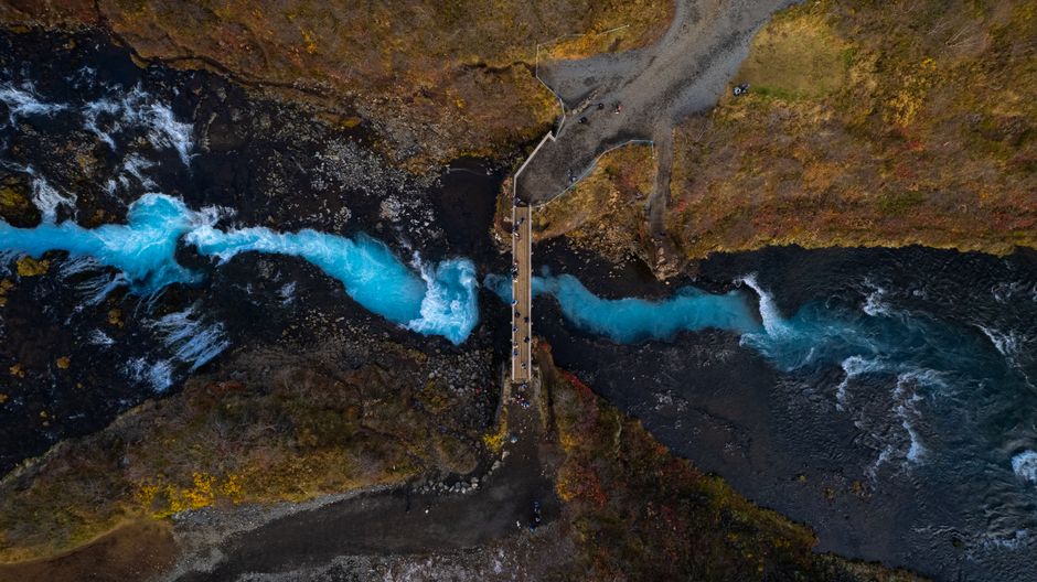 A breathtaking aerial shot of a vibrant blue river winding under a rustic bridge in a natural landscape.
