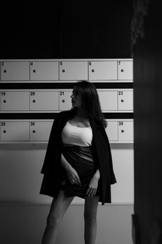 Elegant woman in stylish attire standing indoors with numbered lockers, monochrome aesthetic.