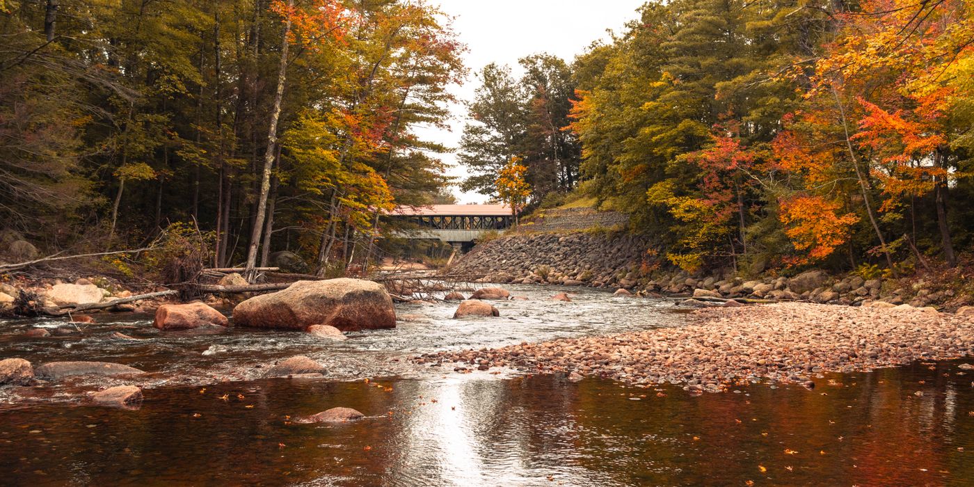 Wooden covered bridge over a river surrounded by autumn foliage in New England