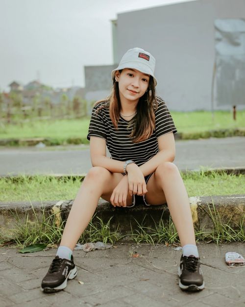 Free Young woman sitting casually on a city street, exuding a relaxed summertime vibe. Stock Photo