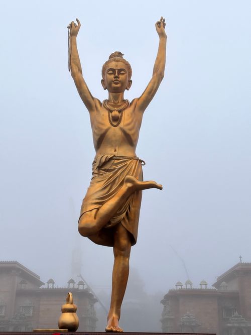 Free A striking golden statue of a dancer stands gracefully amid fog, surrounded by temple architecture. Stock Photo