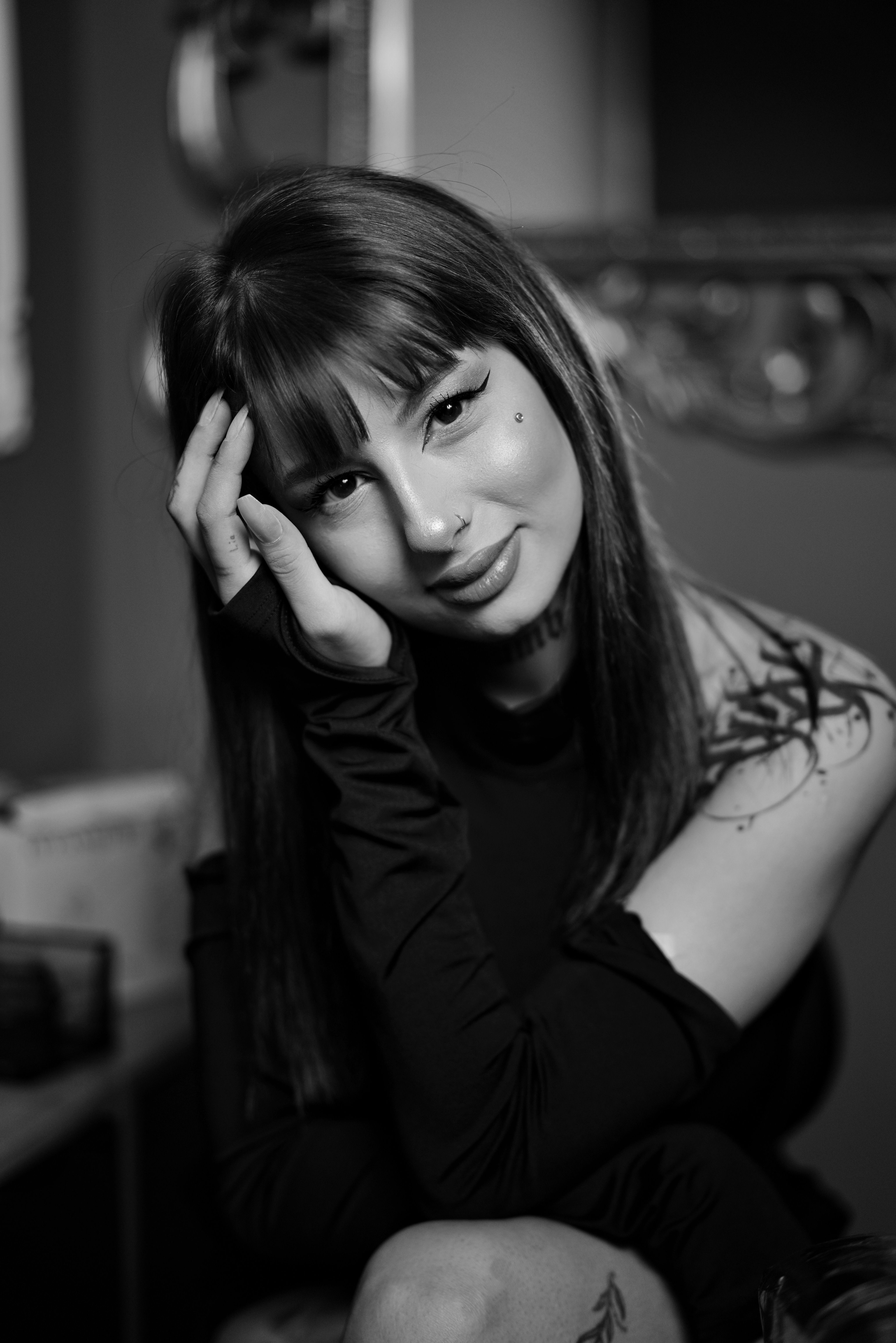 Stylish black and white portrait of a young woman with tattoos, smiling gently.