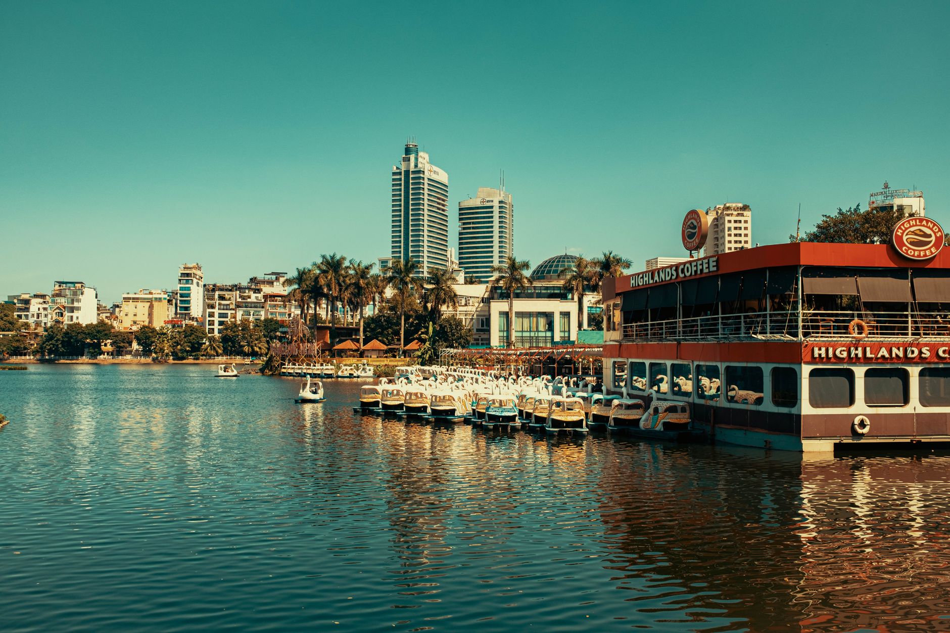 Vibrant Hanoi cityscape featuring skyscrapers, a river, and a floating cafe.