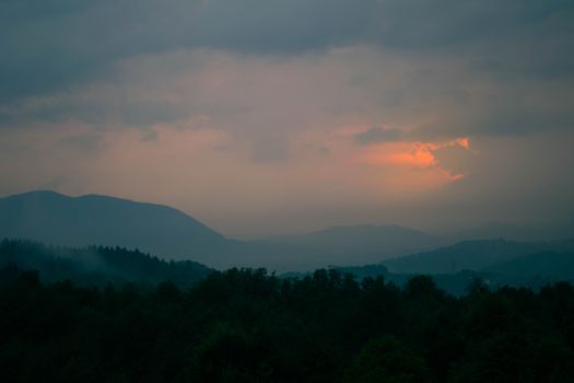 Misty sunset over Sarajevo forests in Bosnia, with moody clouds and distant mountains.