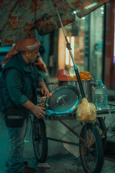 Man selling food on a cart under an umbrella in Bursa's evening street market.