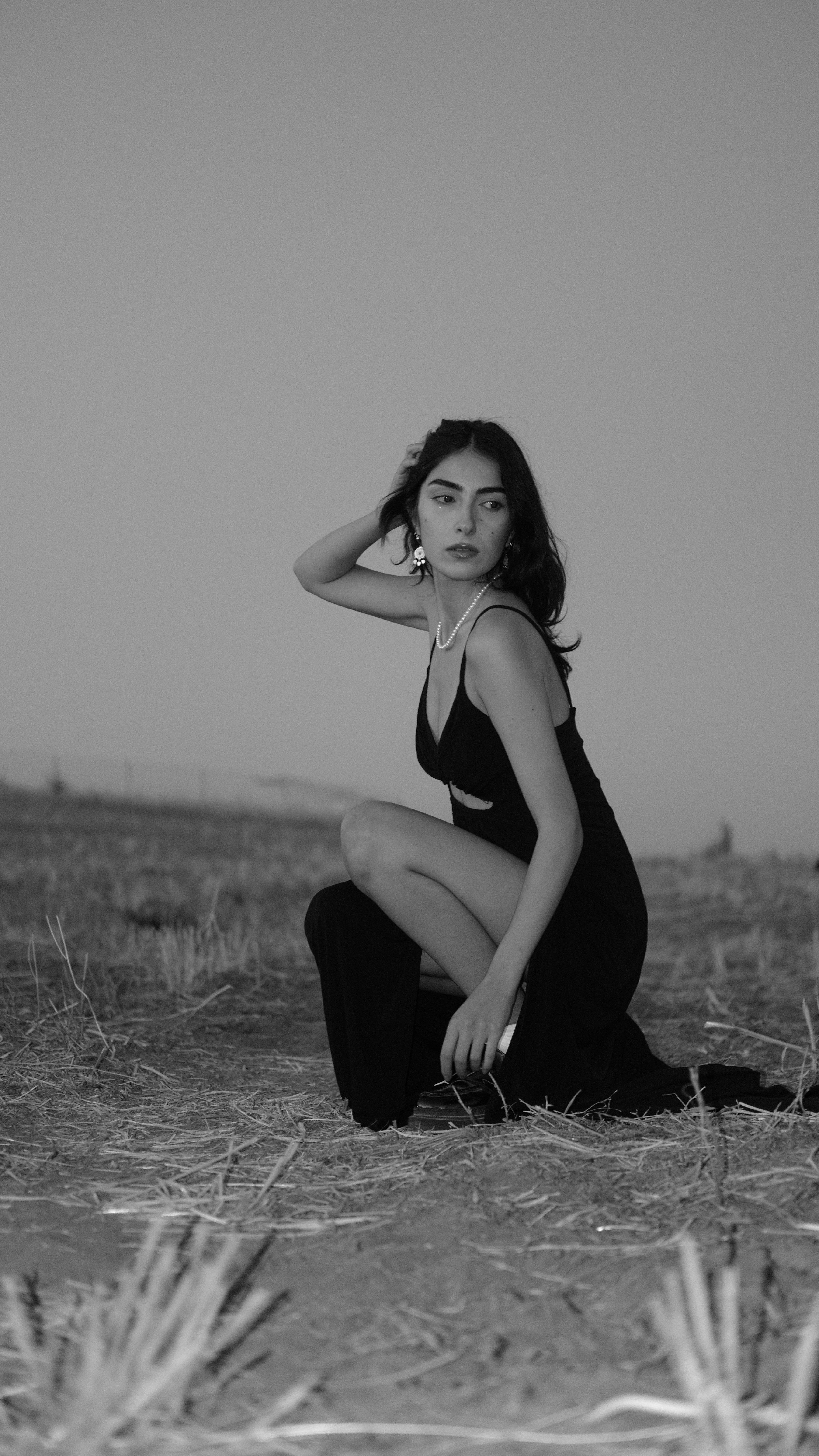 A stylish woman poses gracefully in a black dress in a field during summer.
