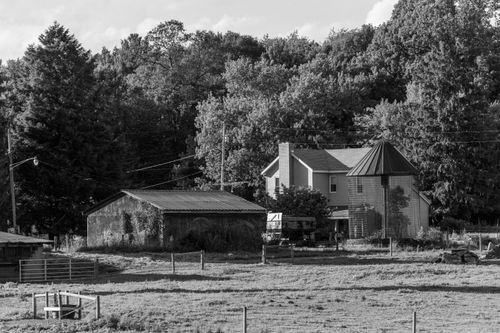 Free A tranquil rural farmhouse surrounded by trees in black and white. Stock Photo
