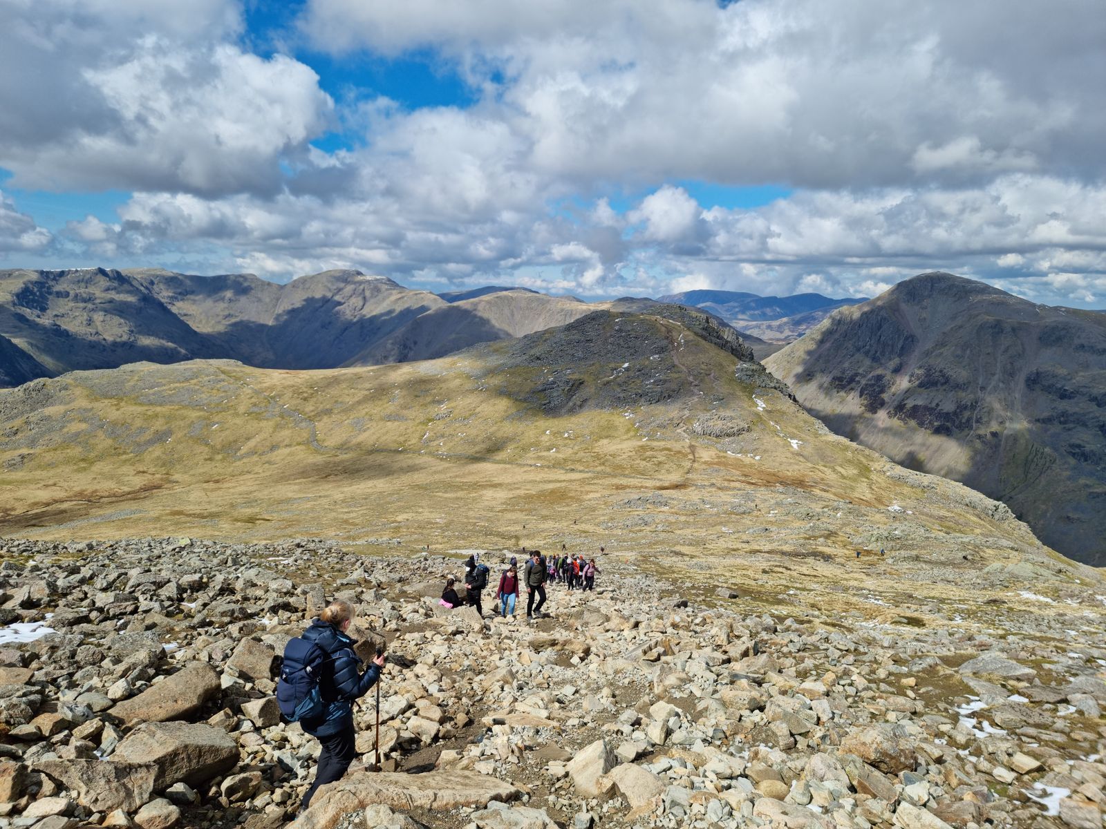 A group in walking gear descending a rocky boulder field high on the Lake District fells.