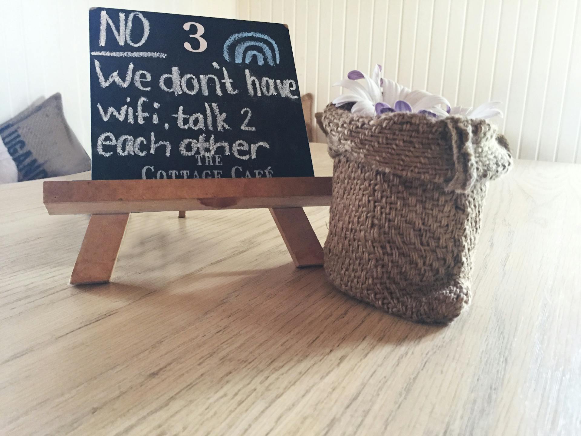 Cozy cafe table setting with a chalkboard sign, burlap sack, and decorative flowers on a wooden table.