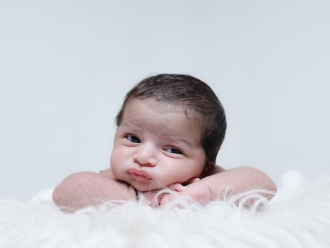 Cute baby posing with a curious expression, lying comfortably on a soft, fluffy blanket. Perfect for family and lifestyle themes.