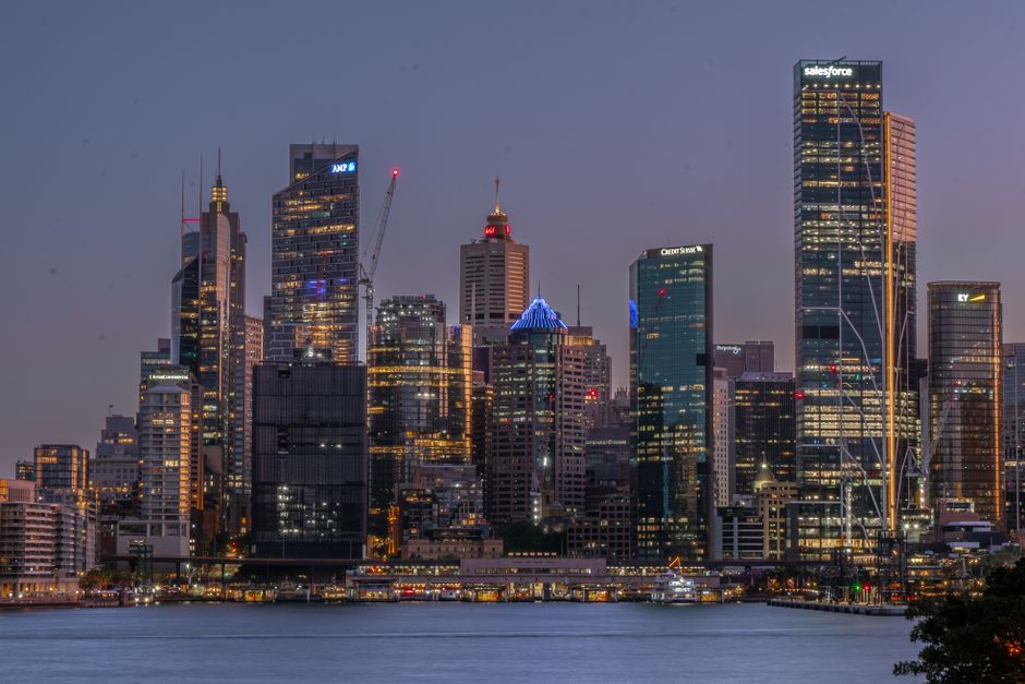 A breathtaking view of Sydney's skyline at twilight with lit skyscrapers reflecting on the water.