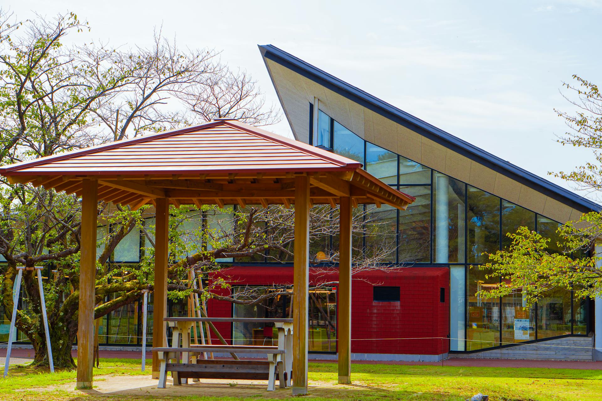 Contemporary building with a slanted roof next to a traditional wooden gazebo in a serene park setting.