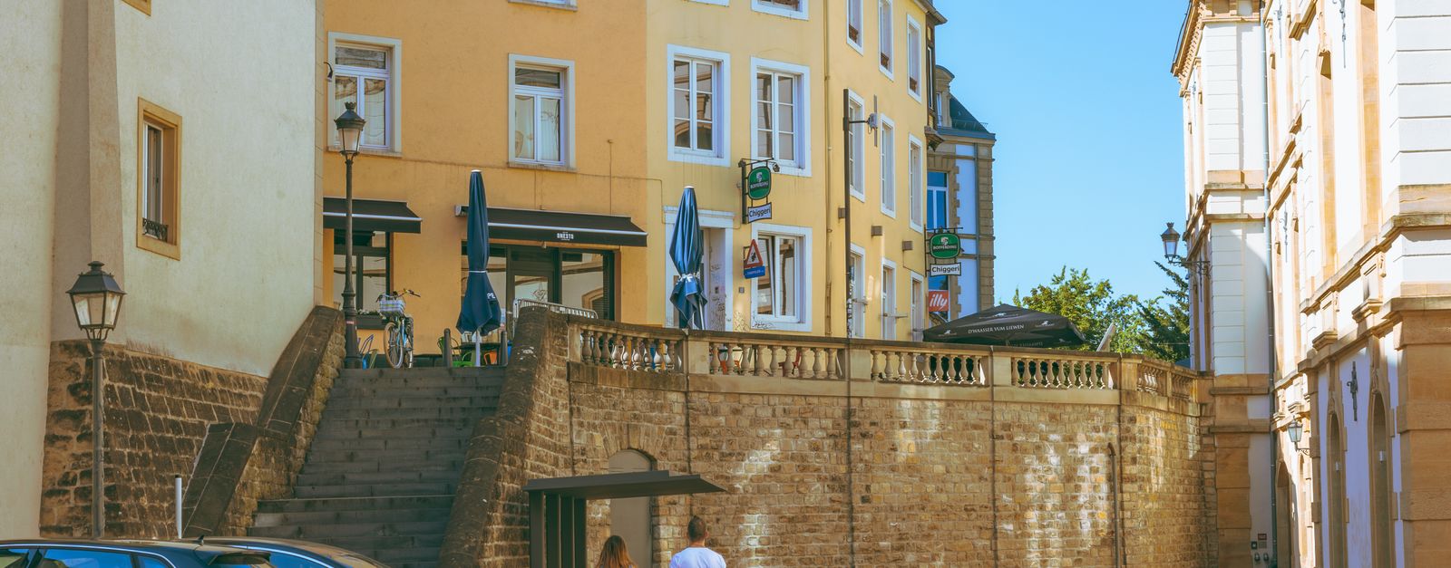 A couple walks along a picturesque street in Luxembourg City, showcasing historic architecture and urban charm.