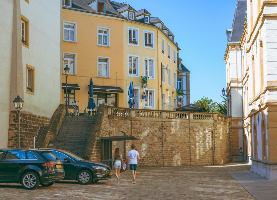 A couple walks along a picturesque street in Luxembourg City, showcasing historic architecture and urban charm.
