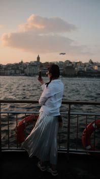 A woman photographs the Istanbul cityscape at dusk from a ferry, capturing the city’s iconic skyline.