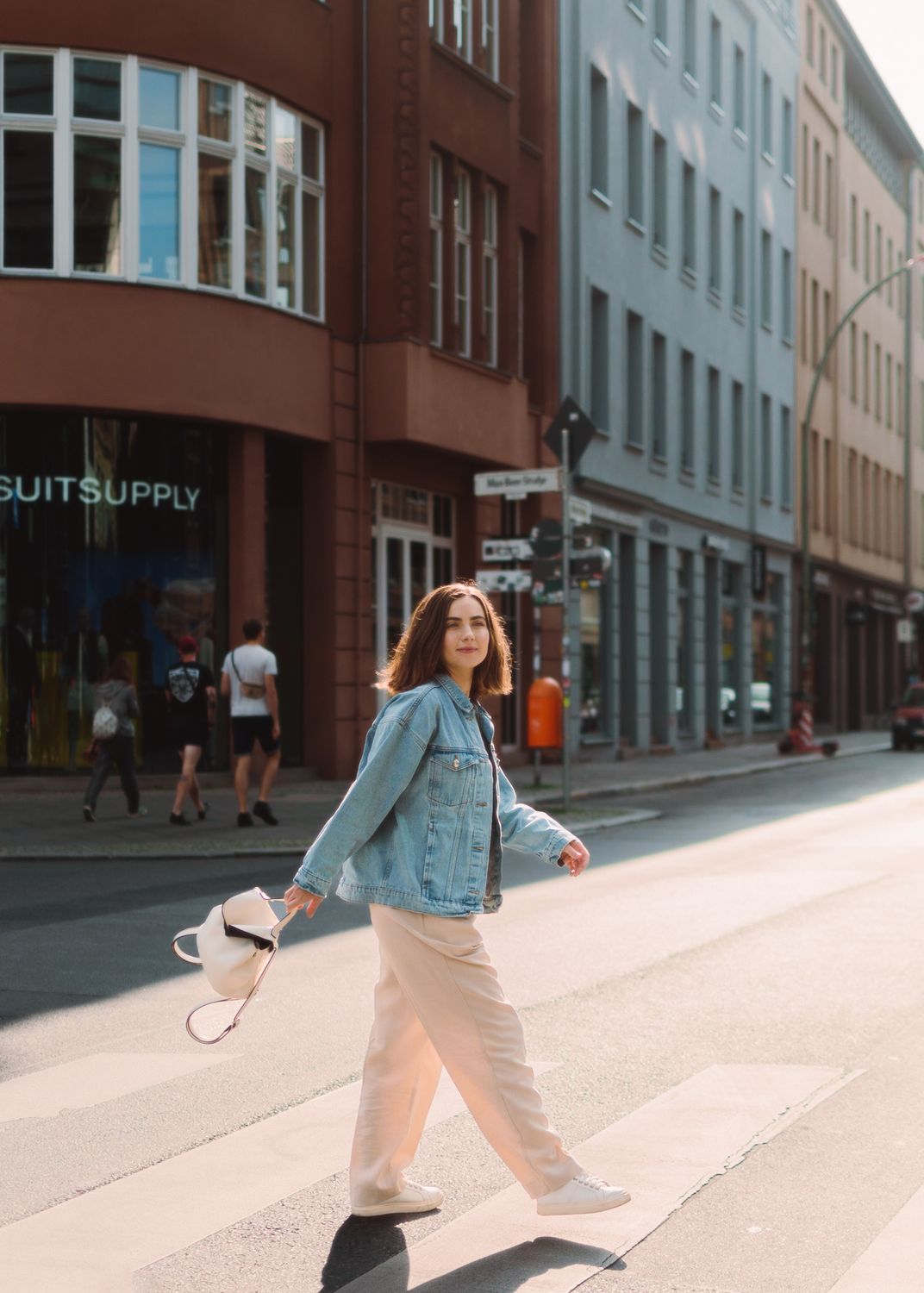 Woman in jean jacket crossing a city street in flats
