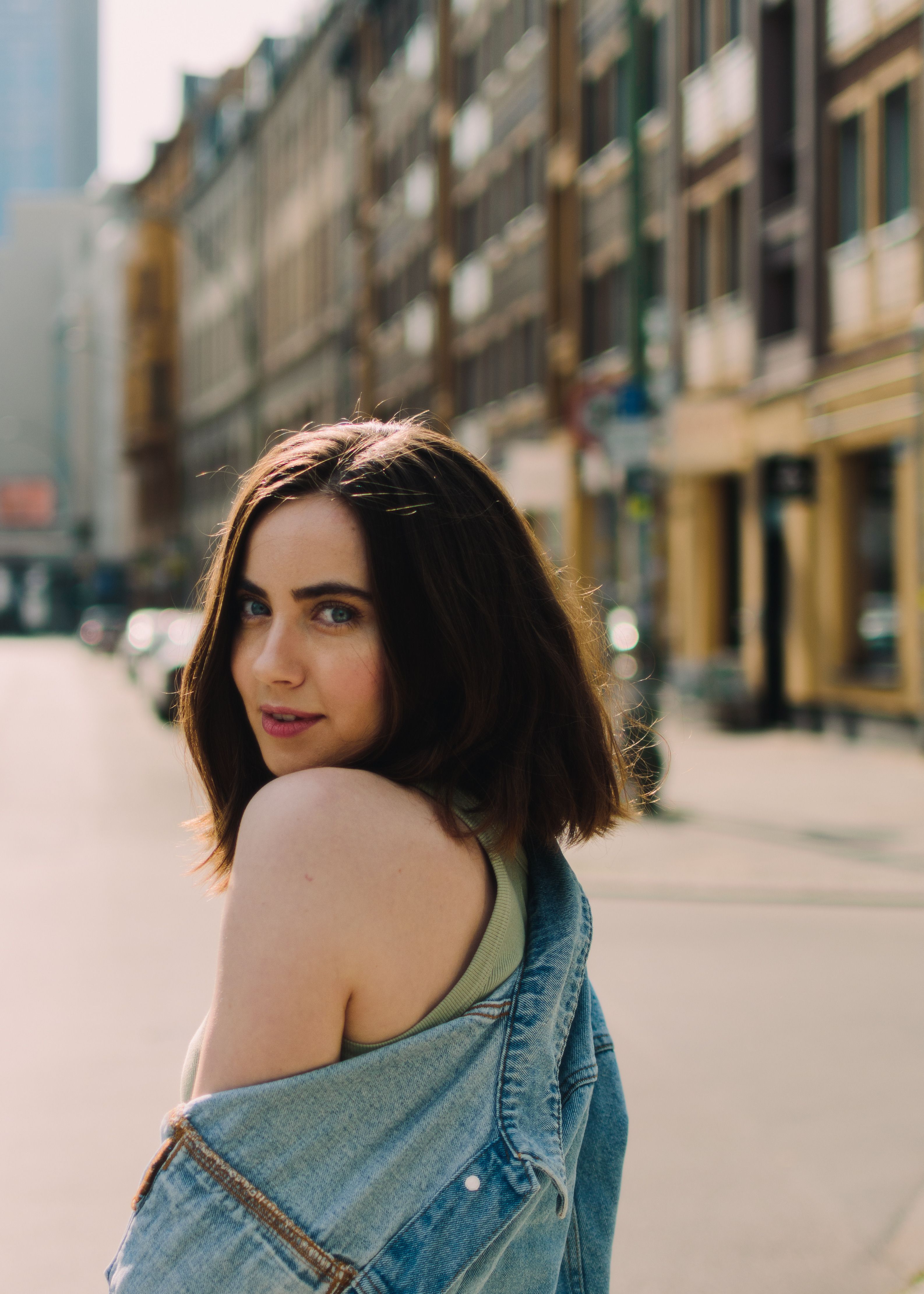 Portrait of a woman in a denim jacket posing on a city street, showcasing a urban lifestyle.
