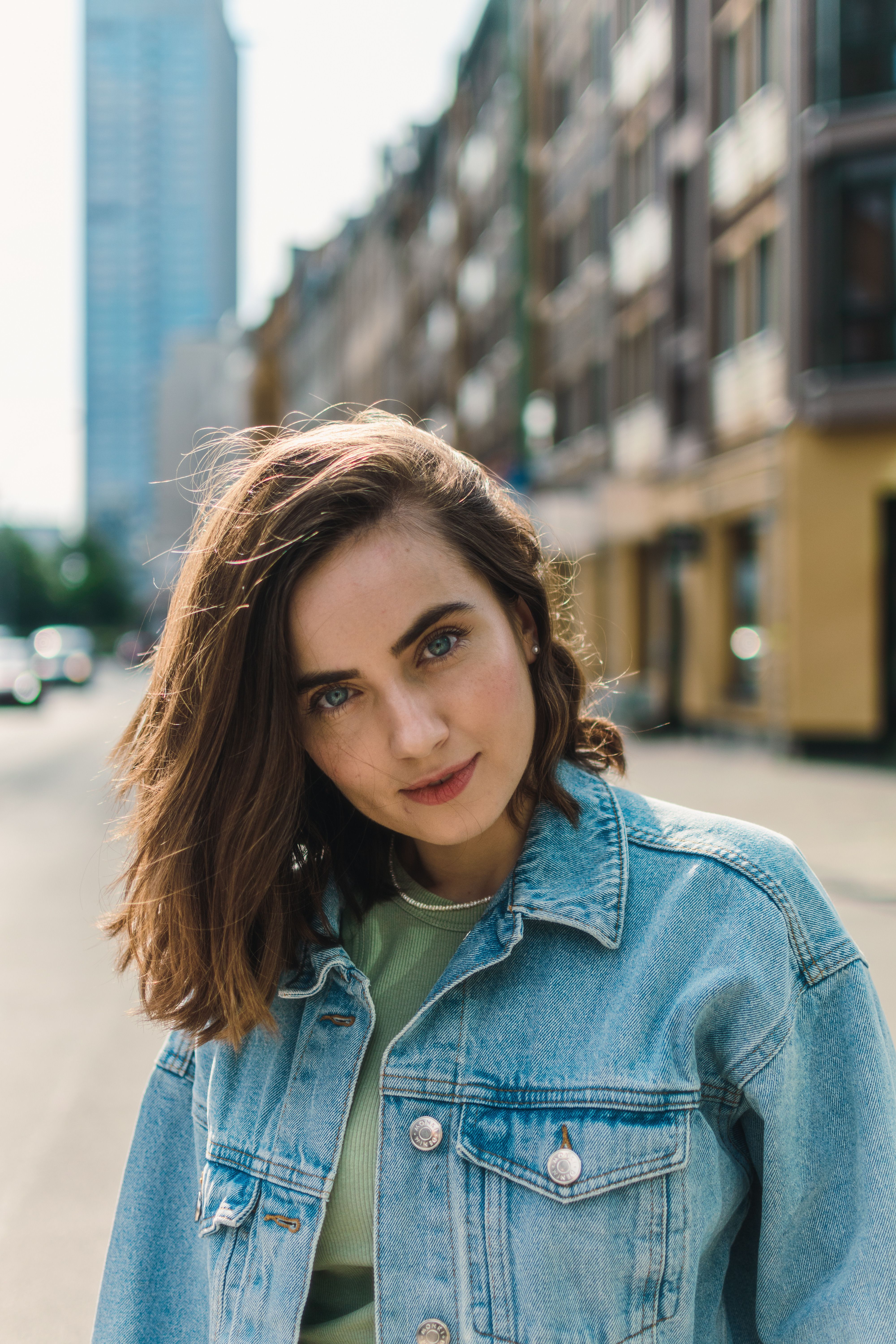Fashionable woman in denim jacket posing on a city street during daytime.
