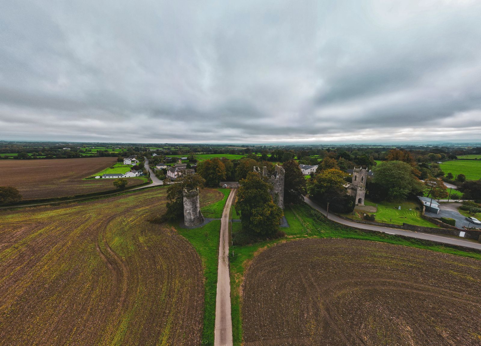 Drone shot of medieval castle ruins surrounded by fields and village in Kilkenny, Ireland