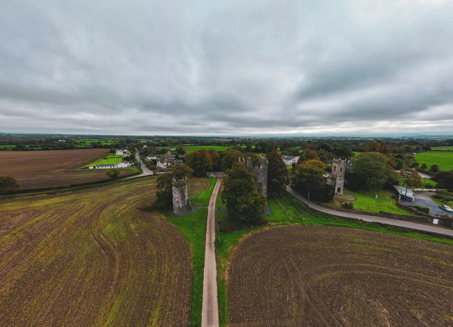 Drone shot of medieval castle ruins surrounded by fields and village in Kilkenny, Ireland.